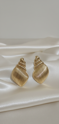 Gold shell-shaped earrings on a white satin surface