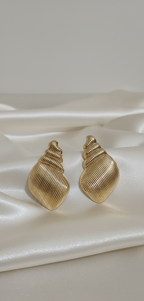 Gold shell-shaped earrings on a white satin surface