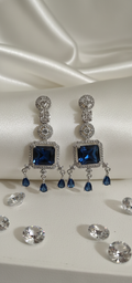 Pair of silver earrings with blue gemstones on a white satin background
