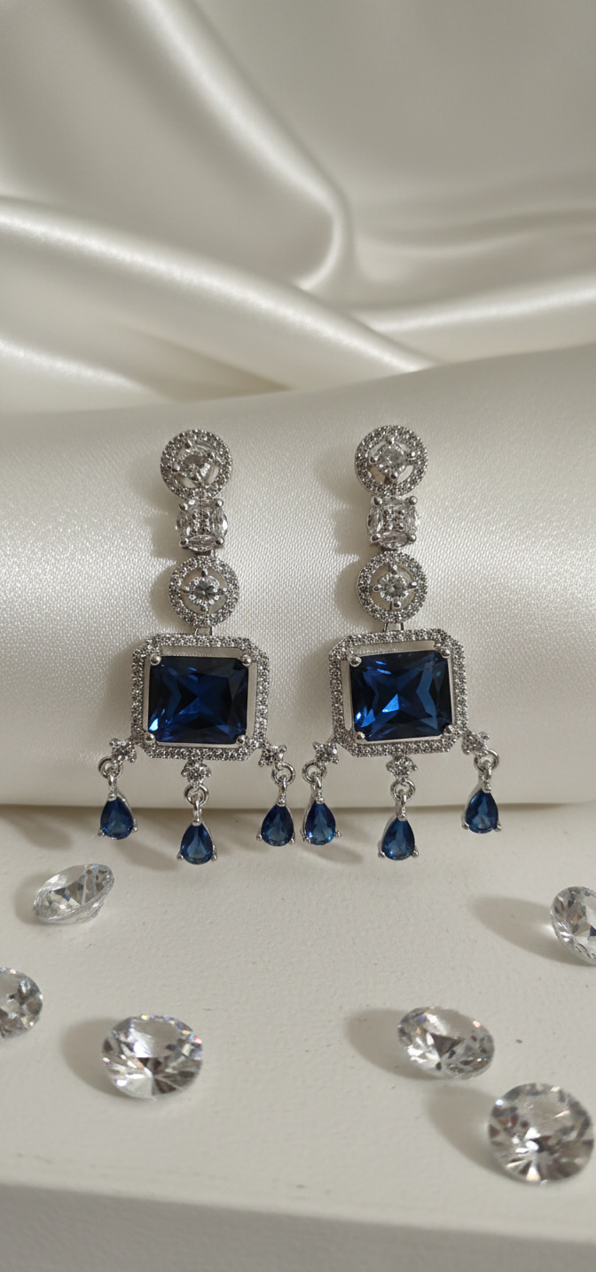 Pair of silver earrings with blue gemstones on a white satin background