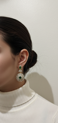 Close-up of a person wearing a pair of earrings with green gemstones against a plain background.