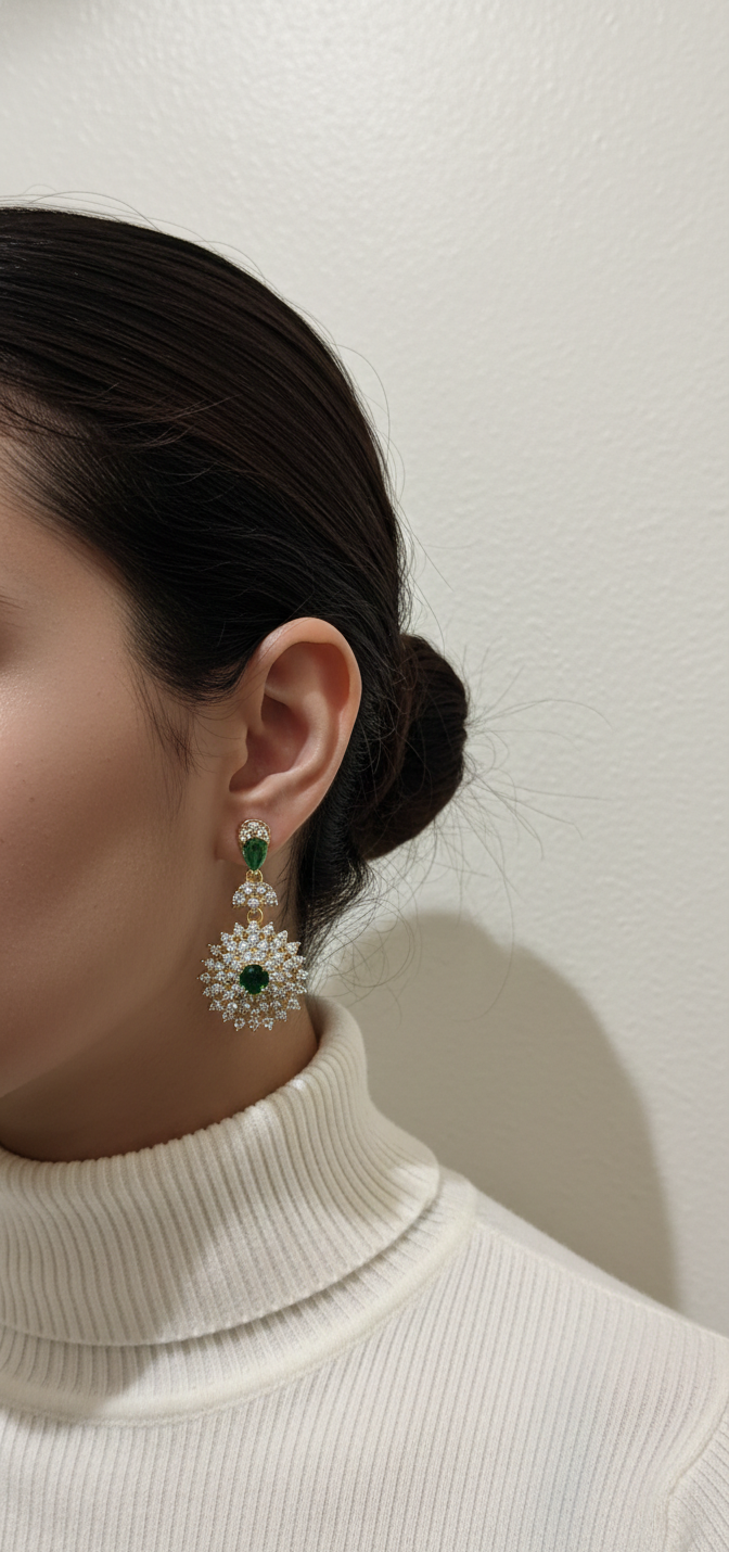 Close-up of a person wearing a pair of earrings with green gemstones against a plain background.