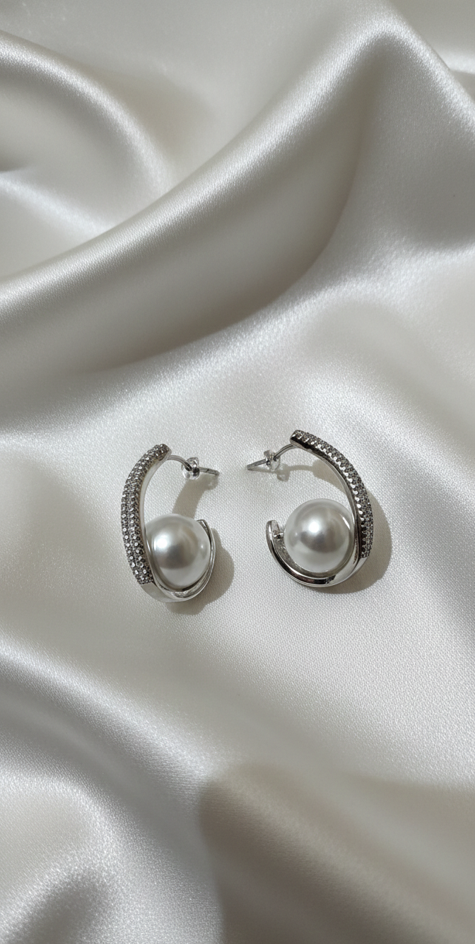 Pair of silver hoop earrings with pearls on a satin surface