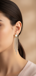 Close-up of a woman wearing a star-shaped earring with tassels against a beige background
