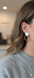 Close-up of a person wearing pearl and gold hoop earrings with a blurred indoor background.