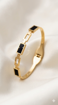 Gold bracelet with black square stones on a light background