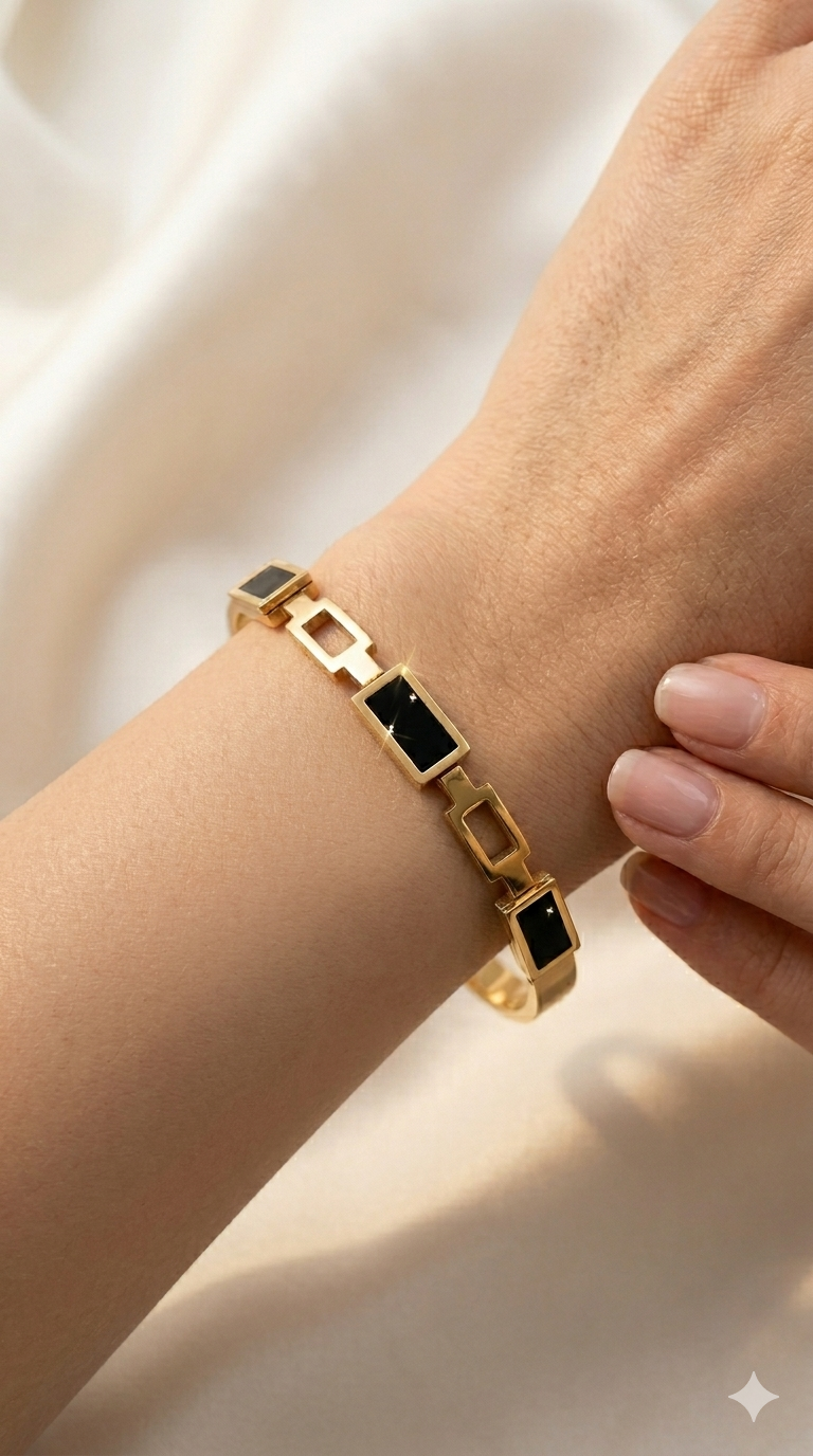 Gold bracelet with black stones on a wrist against a neutral background