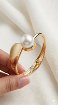 Gold bracelet with a pearl held by a hand on a beige fabric background