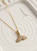 Gold necklace with a whale tail pendant on a white textured surface