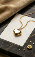 Gold heart-shaped pendant necklace on a marble surface with gold dust