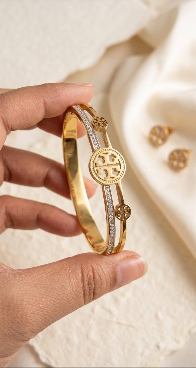 Gold bracelet with a circular design held by a hand against a beige fabric background