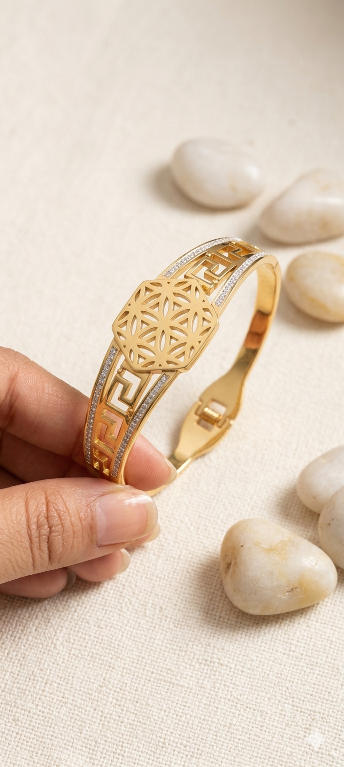 Gold bracelet with intricate design held by a hand on a light background
