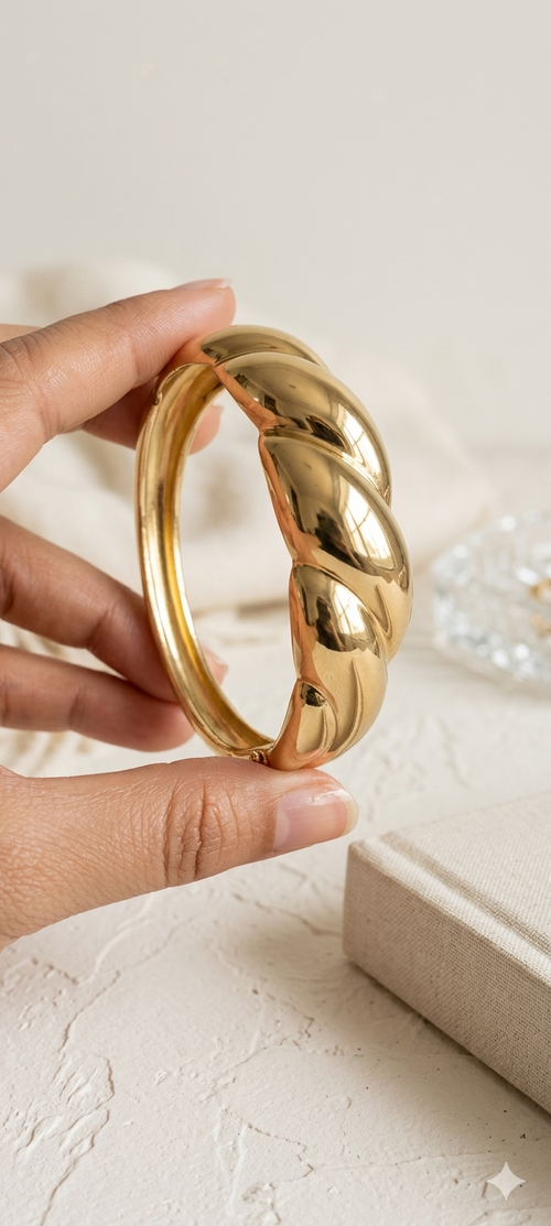 Gold bangle held by a hand on a light background