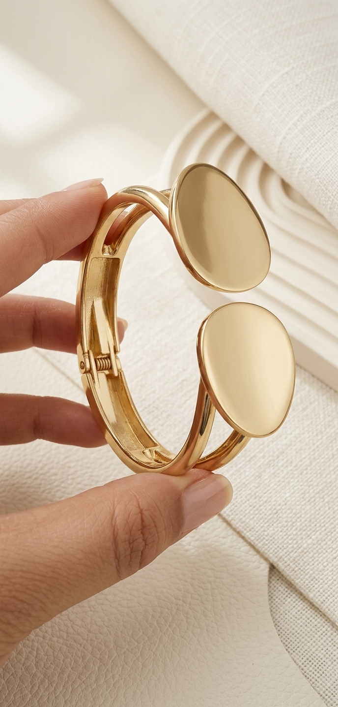 Gold bracelet with oval-shaped clasps held by a hand on a light background