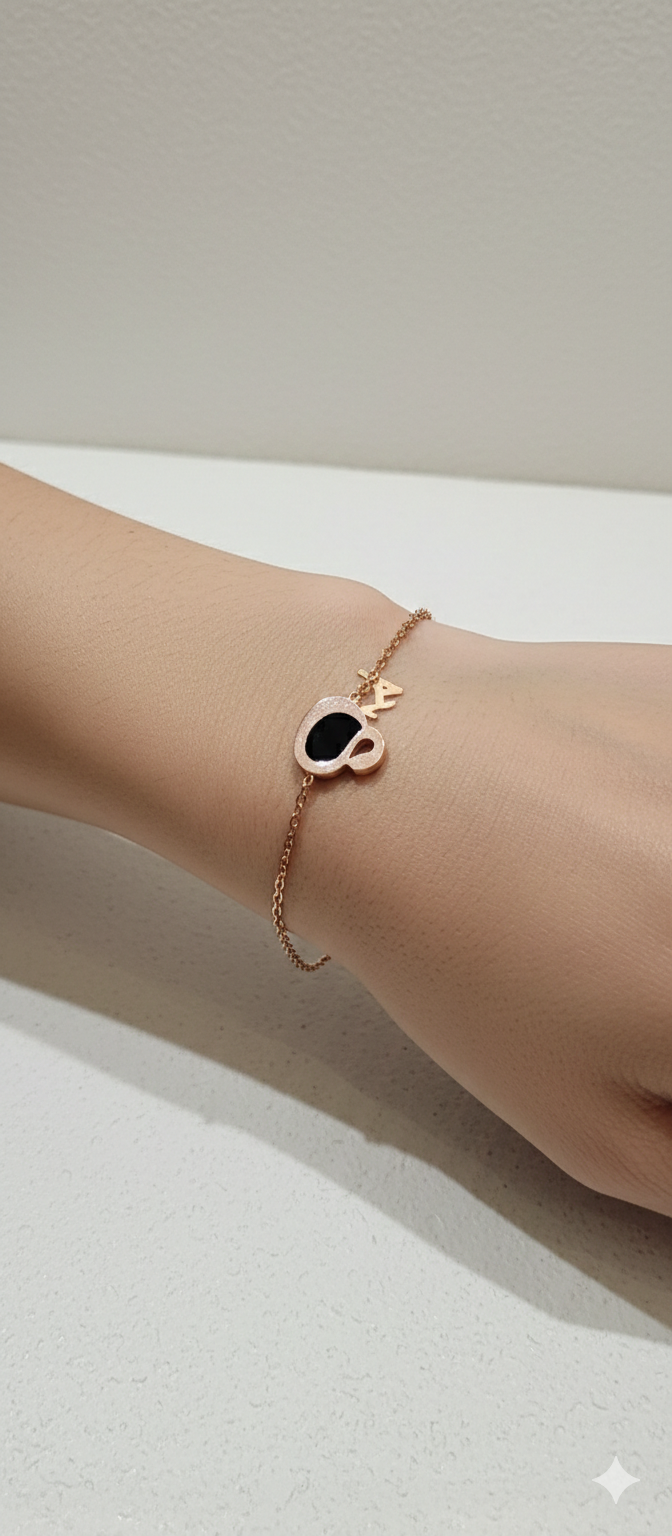 Rose gold bracelet with a heart-shaped black stone on a wrist against a neutral background