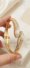 Gold bracelet with pearls and crystals held by a hand on a light background