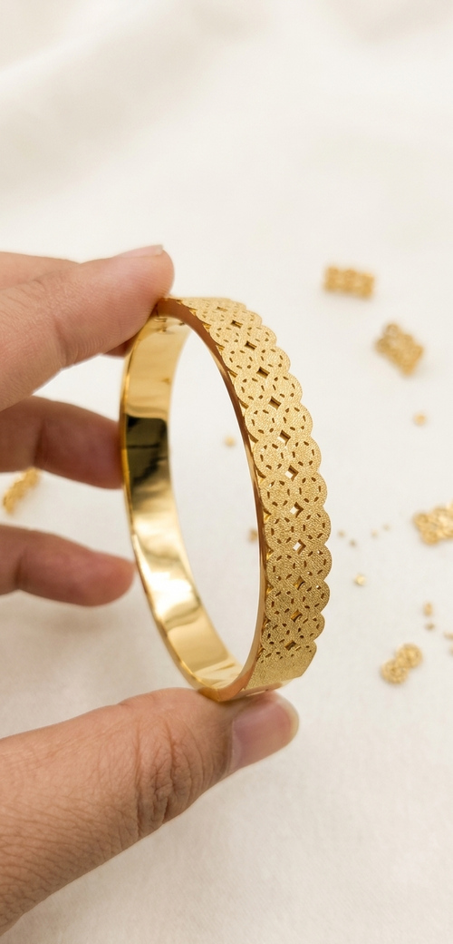 Gold bracelet held by a hand with a light background