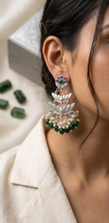 Close-up of a person wearing intricate earrings with green gemstones on a neutral background.