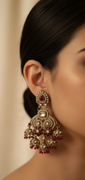 Close-up of a woman wearing a pair of ornate earrings with red stones against a neutral background