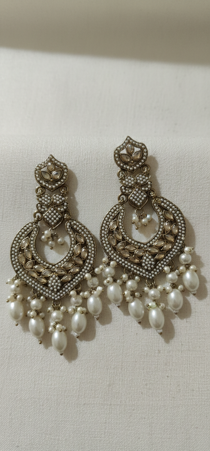 Pair of ornate earrings with pearl drops on a light background
