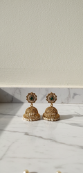 Gold jhumka earrings with green gemstones on a marble surface with a white background