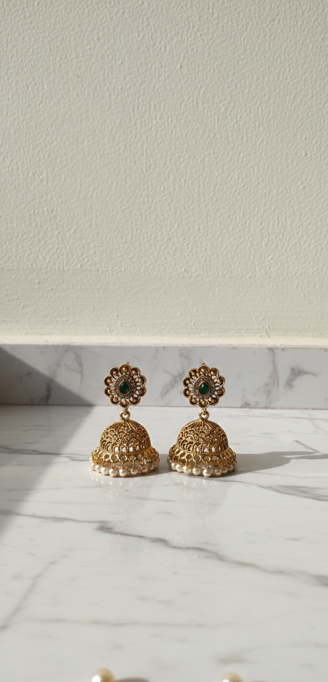 Gold jhumka earrings with green gemstones on a marble surface with a white background
