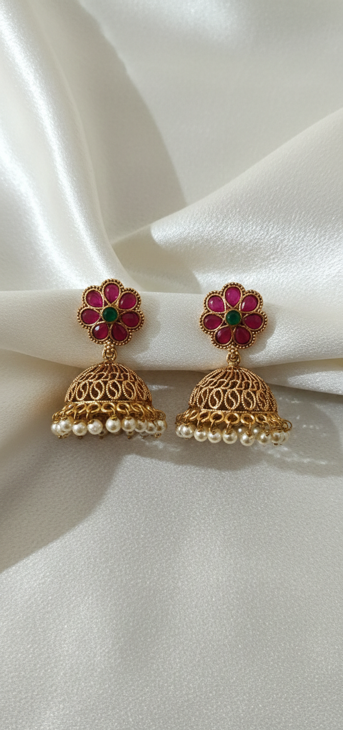 Gold earrings with red and green gemstones on a white fabric background