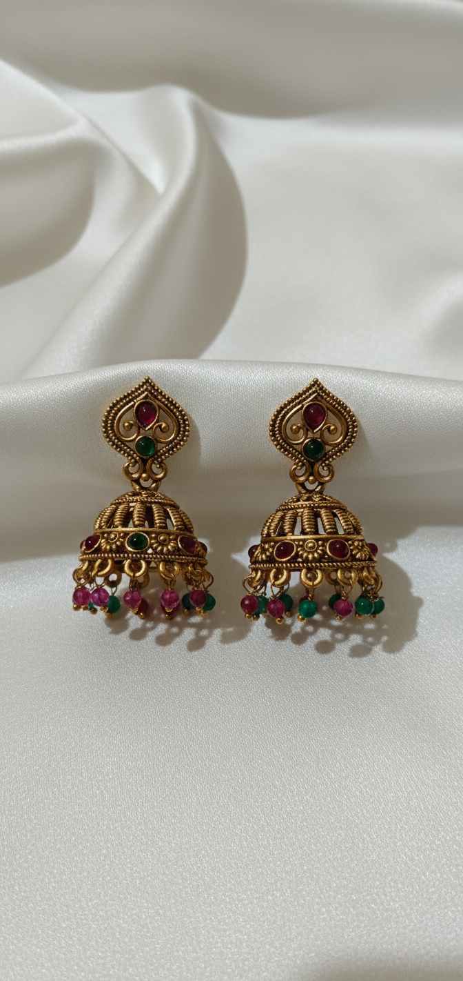 Pair of gold earrings with red and green stones on a white fabric background