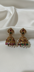 Pair of gold earrings with red and green stones on a white fabric background
