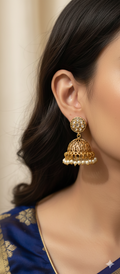 Gold earrings with pearls worn by a person in a blue saree against a beige background