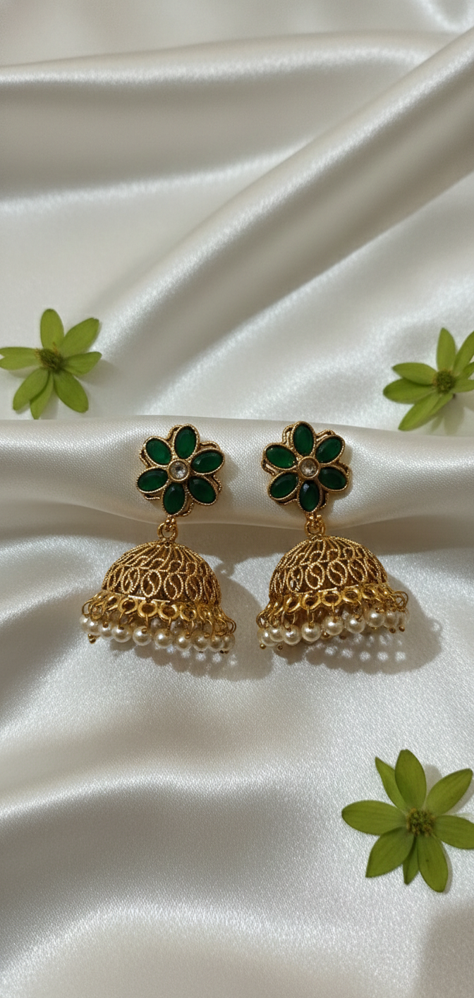 Gold and green floral earrings on a white fabric background with green flowers.